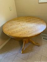 Round oak pedestal table against wall showing top and base