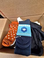 Box showing new Bombas navy socks beside orange polka-dot and other patterned socks