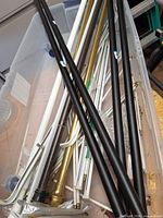 Plastic tote containing multiple black, white, brass and silver curtain rods of varying lengths and styles