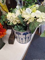 Metal pail planter with cream hydrangea artificial flowers beside wooden clothes tree base
