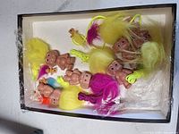 box containing troll dolls with yellow, magenta and rainbow hair plus small brown bubble heads