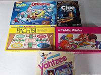 Five boxed games stacked: Operation, Clue Escape, Pachisi, Tiddly Winks, Mickey Mouse Yahtzee