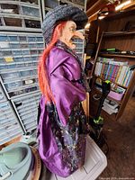 Side view of witch prop showing purple robe, red hair, black hat, broom