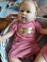 Blond baby doll wearing pink "PRINCESS" romper seated in white wicker basket