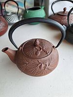 Full view of brown cast iron teapot showing pine cone relief and handle