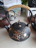 Full view of black cast iron floral teapot with handle and decorative design
