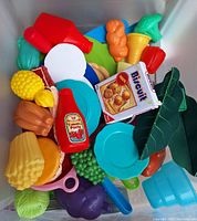Top view of Sterilite bin filled with plastic toy food pieces and blue plates