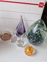 Group of paperweights: purple teardrop, two clear droplets, green swirl egg, millefiori, orange floral