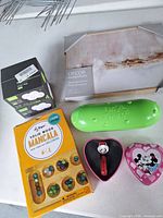 Group shot of all items: wristwatch in case, Mickey tin, Mancala game box, In A Pickle container, cloud graphics game box, wall art