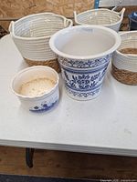 Three rope and jute baskets, large and small blue-and-white ceramic planters on table