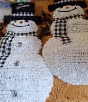 Two white tinsel snowman wall decorations with gingham scarves and top hats