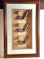 Front view of framed golf wedge history display showing club heads, balls and labels