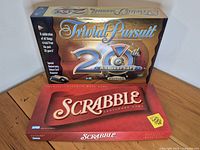 Sealed retail boxes of Trivial Pursuit 20th Anniversary Edition and Scrabble displayed on tabletop