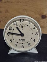 Front view of Cosmo Time wind-up alarm clock showing dial and hands