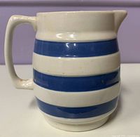 Side view of blue and white striped ceramic cream jug showing handle, spout and stripe pattern
