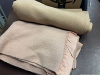 Rolled beige blanket beside folded pink blanket with satin edge