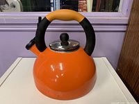 Front view of orange Prestige tea kettle showing body, handle, lid, and spout