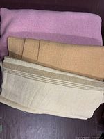 Three folded wool blanket pieces in cream, brown, and pink