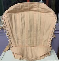 Full view of peach corset laid flat showing boning and side lacing