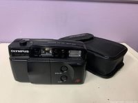 Front view of Olympus Trip AF 20 camera with soft case beside it