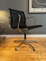 Left side perspective of the black mesh Eames EA108 chair showing armrest, seat, backrest and four-star base