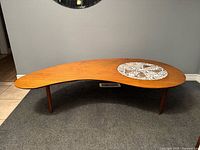 Full view of kidney-shaped coffee table showing wood surface, mosaic inset and three legs