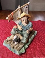 Front view of entire porcelain figurine showing man on raft with dog and sail