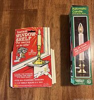 Front view of boxed automatic candle beside boxed window shelf kit
