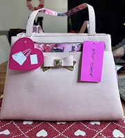 Front view of blush pink Betsey Johnson satchel with bow hardware and heart tag
