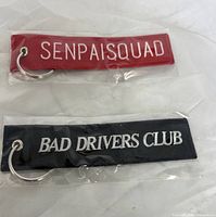 Both keychains in plastic packaging showing slogans and rings