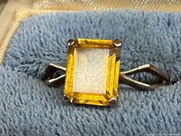 Close-up of synthetic yellow stone in prong setting on blue ring box cushion