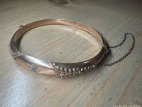 Full view of gold hinged bangle showing overall form and safety chain