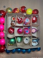 Overall view of cardboard box with assorted mercury glass ornaments and additional ornaments arranged around edges