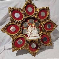 Full view of starburst wall plaque showing gold frame, red velvet panels, mirrors, central porcelain couple