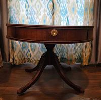 Side view of round mahogany drum table on four-leg pedestal with brass claw feet