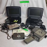 Group shot showing two portable DVD players, three cameras, remotes and cables