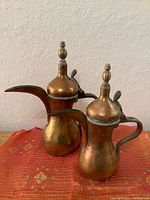 Front view of both brass Dallah pots showing spouts, lids and handles