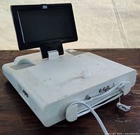 Angled rear view showing flip-down LCD, AV ports, power cord, mounting bracket