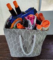 Grey rope-handled bin filled with assorted Nerf blasters and magazines