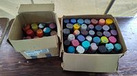 Two cardboard boxes filled with assorted spray paint cans