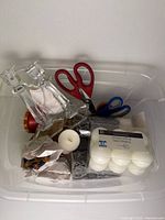 Overview of items inside the clear bin including candlesticks, scissors, candles, decor pieces