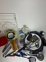 Entire assortment spread on surface showing utensils, plates, bowls, tumblers, stein, linens, wire rack