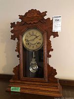 Front view of carved wood Ansonia mantle clock showing dial and pendulum