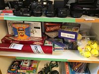 Shelf showing Speak Out, Scrabble, Tic-Tac-Toe sets, red rolled mat, card decks, stress balls