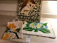 All three tea towels displayed; framed owl towel upright, two folded towels with yellow and white flower prints