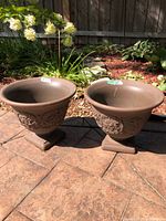 Pair of brown resin pedestal urn planters side by side on patio