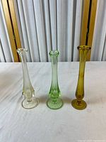 Front view of three glass bud vases in clear, green and amber