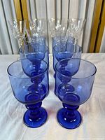 Front view of eight cobalt blue goblets with six clear cut crystal wine glasses behind
