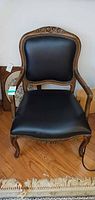 Full front view of black faux leather armchair with carved wood frame