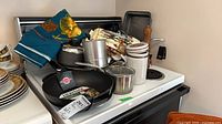 All items piled on stove: cookware, canister, pepper mill, tea towels